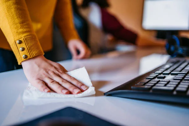 Woman in a yellow long sleeved jumper wiping an office desk with a paper towel